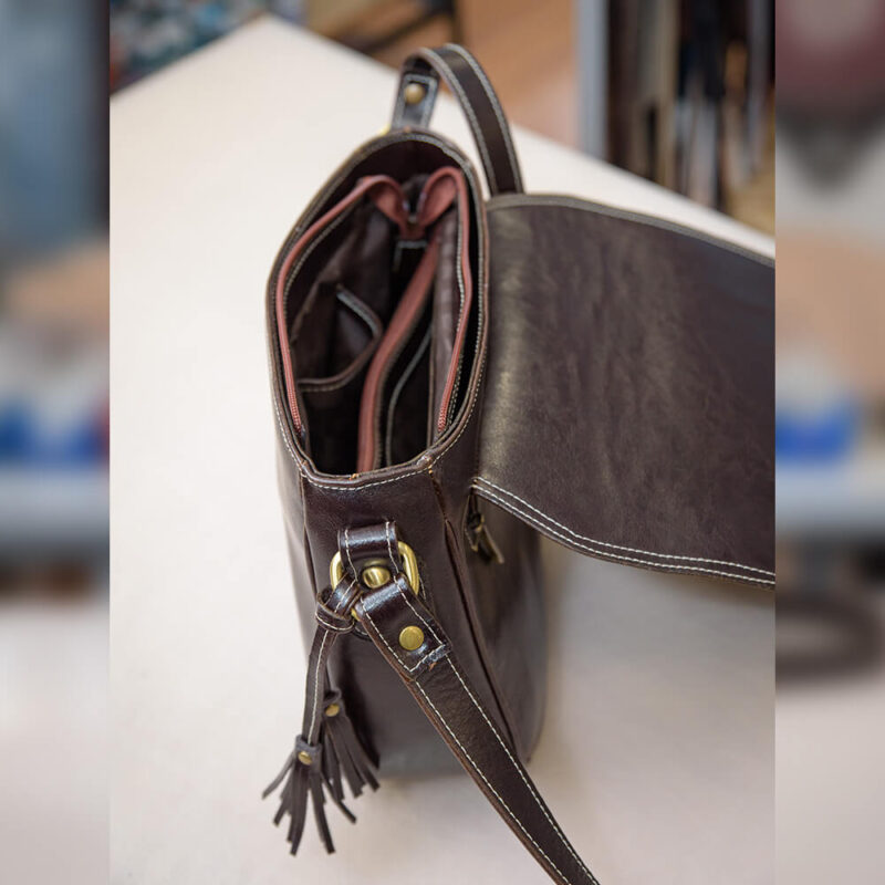 O geantă maro de tip poștaș, cu un aer clasic și funcțional, potrivită pentru a purta cu stil